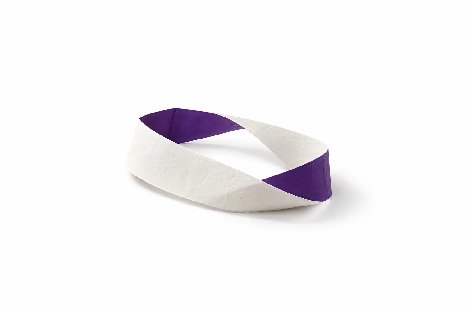 Ein Möbiusband aus weißem Papier liegt am Boden. Wo die Rückseite nach der Drehung nach oben zeigt, ist es violett.